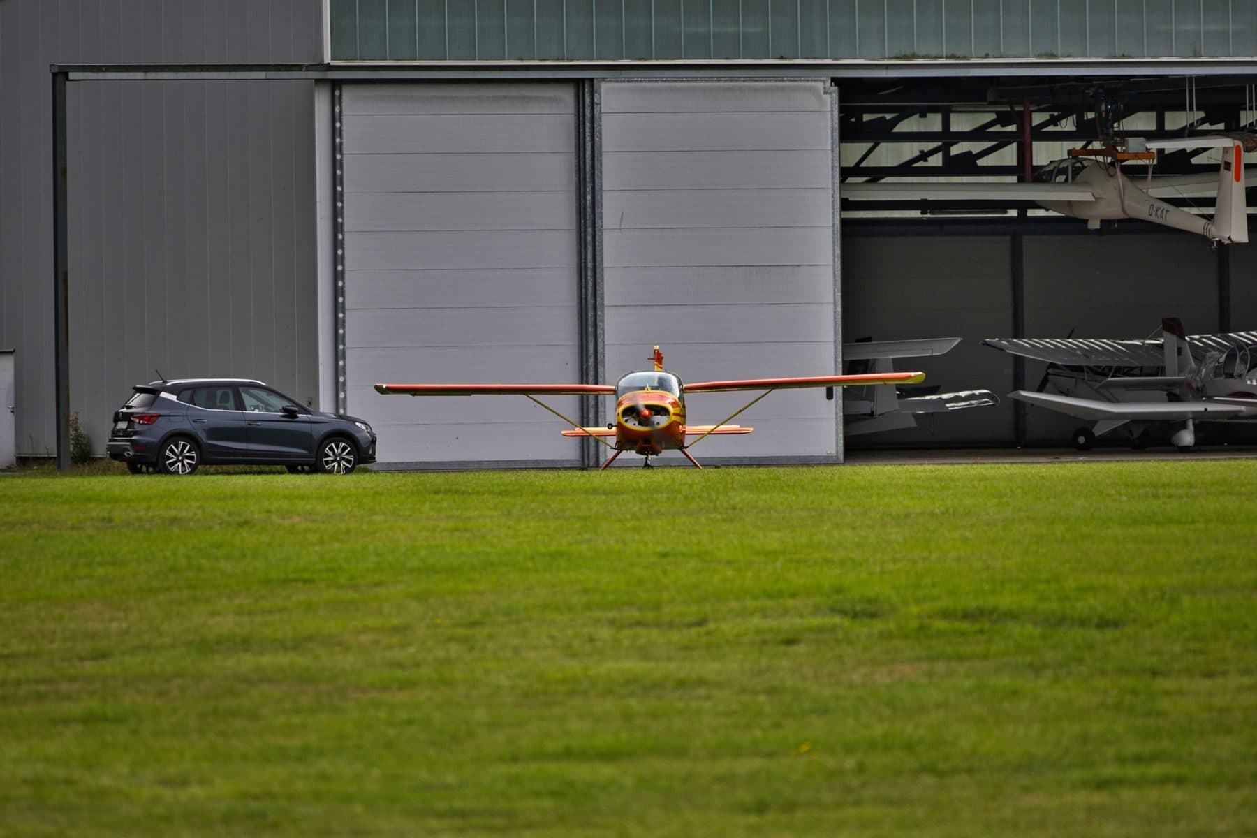A small single-engine plane on grass in front of an open hangar.