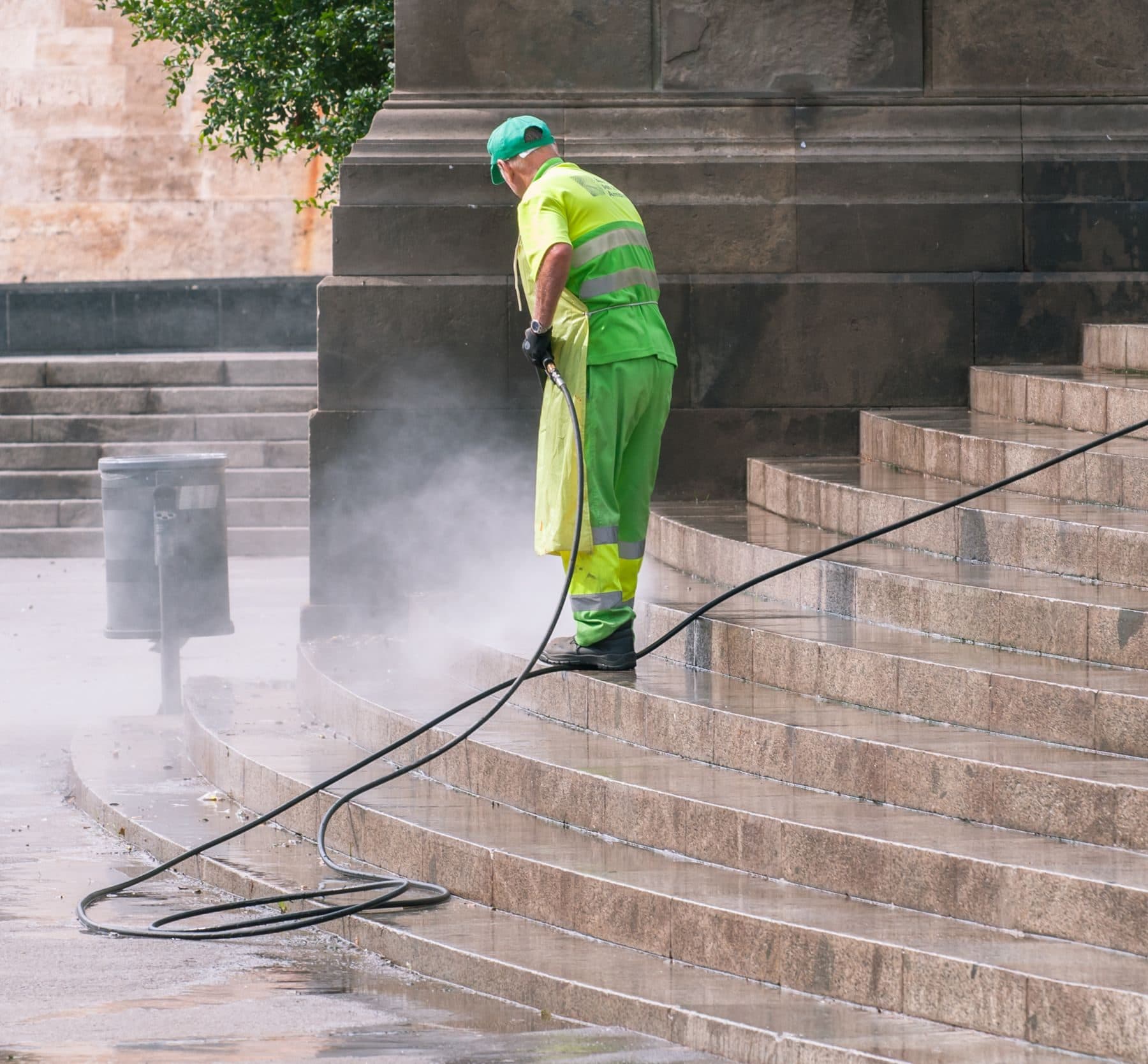 A worker in high-visibility clothing pressure washing stone steps.