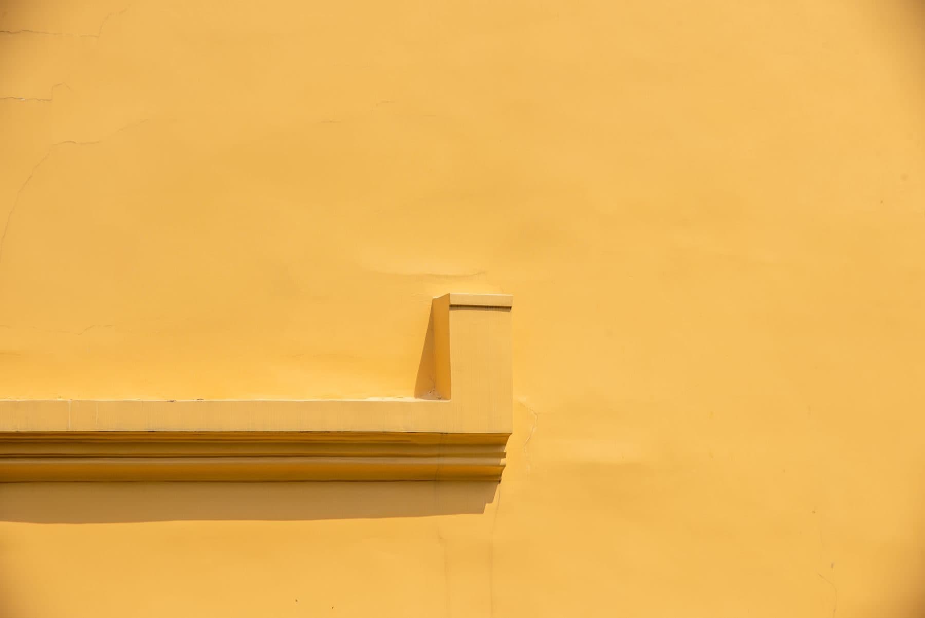 A plain yellow stucco wall with a small ledge, in strong sun.