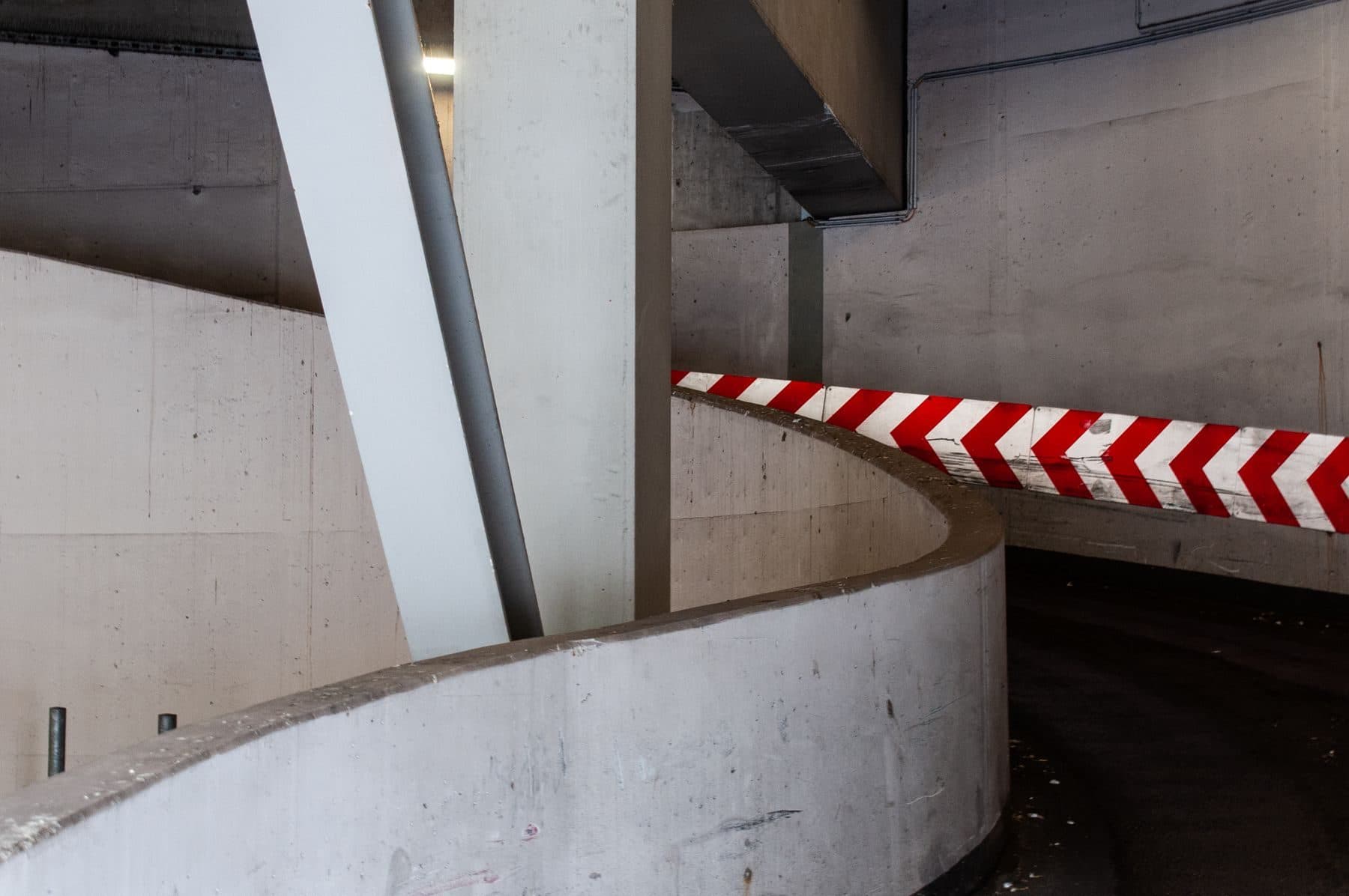 A concrete ramp inside a parking structure with red and white chevron markings.