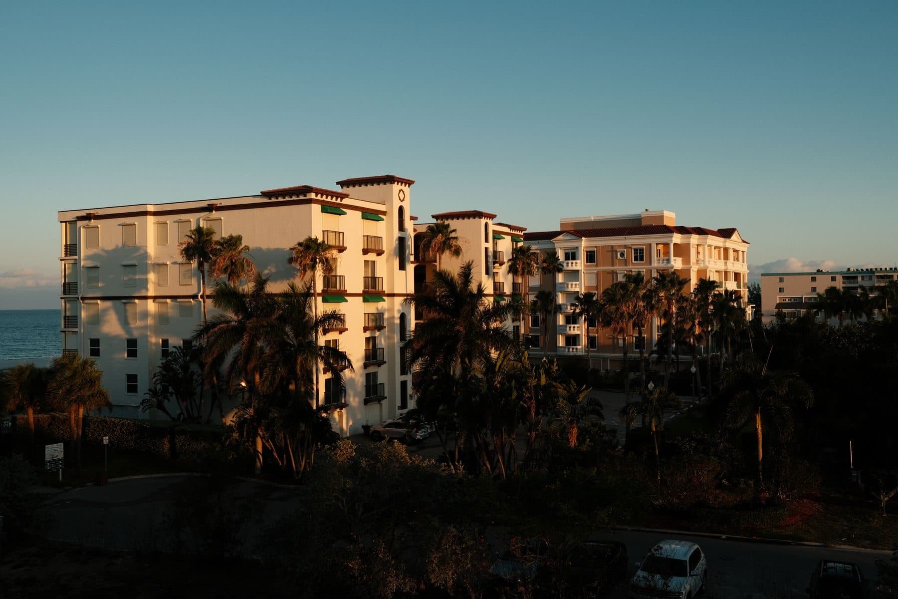 Cream mid-rise buildings with tiled roofs behind palm trees at sunset in Florida.