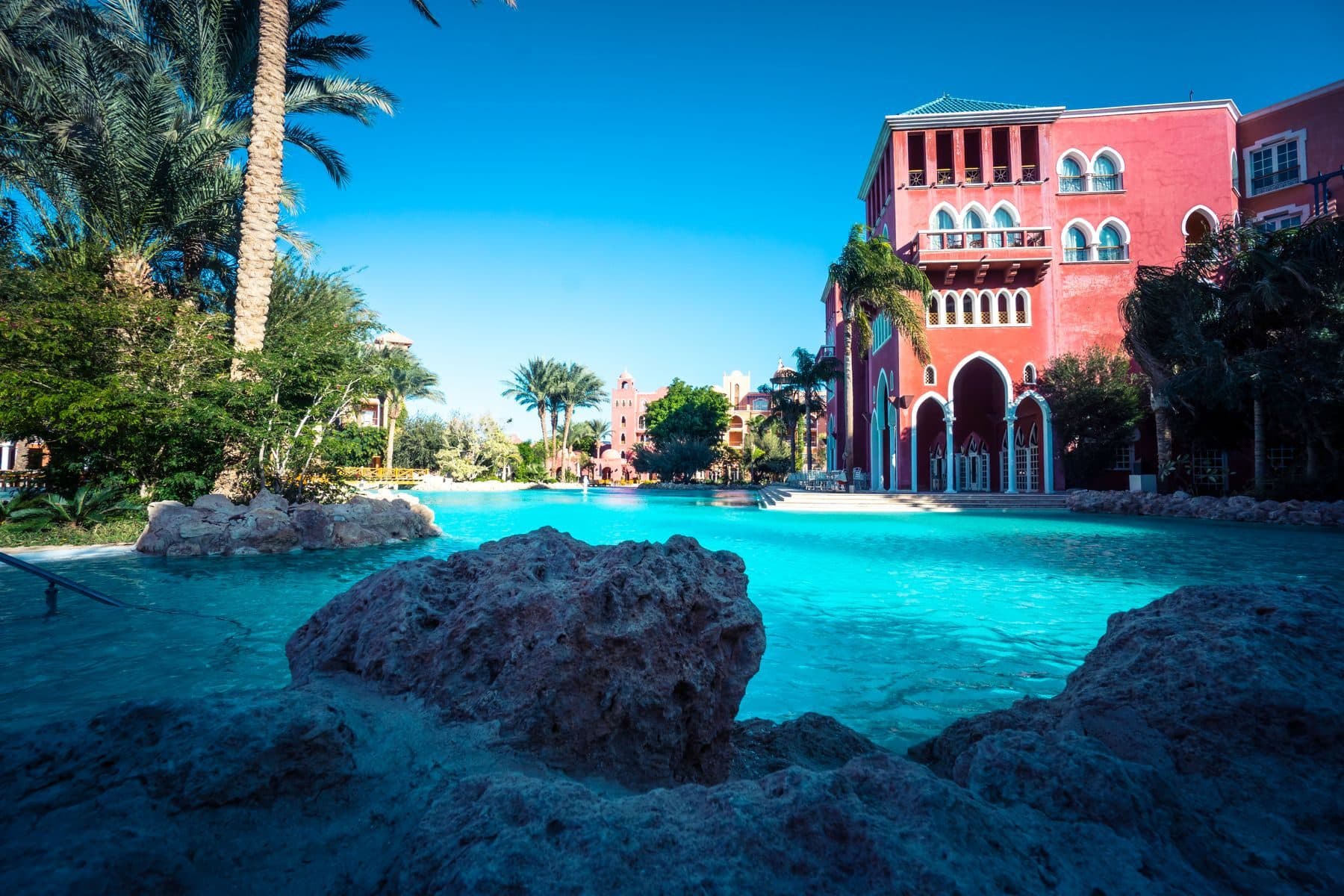 A resort pool with palm trees and a pink hotel building behind it.