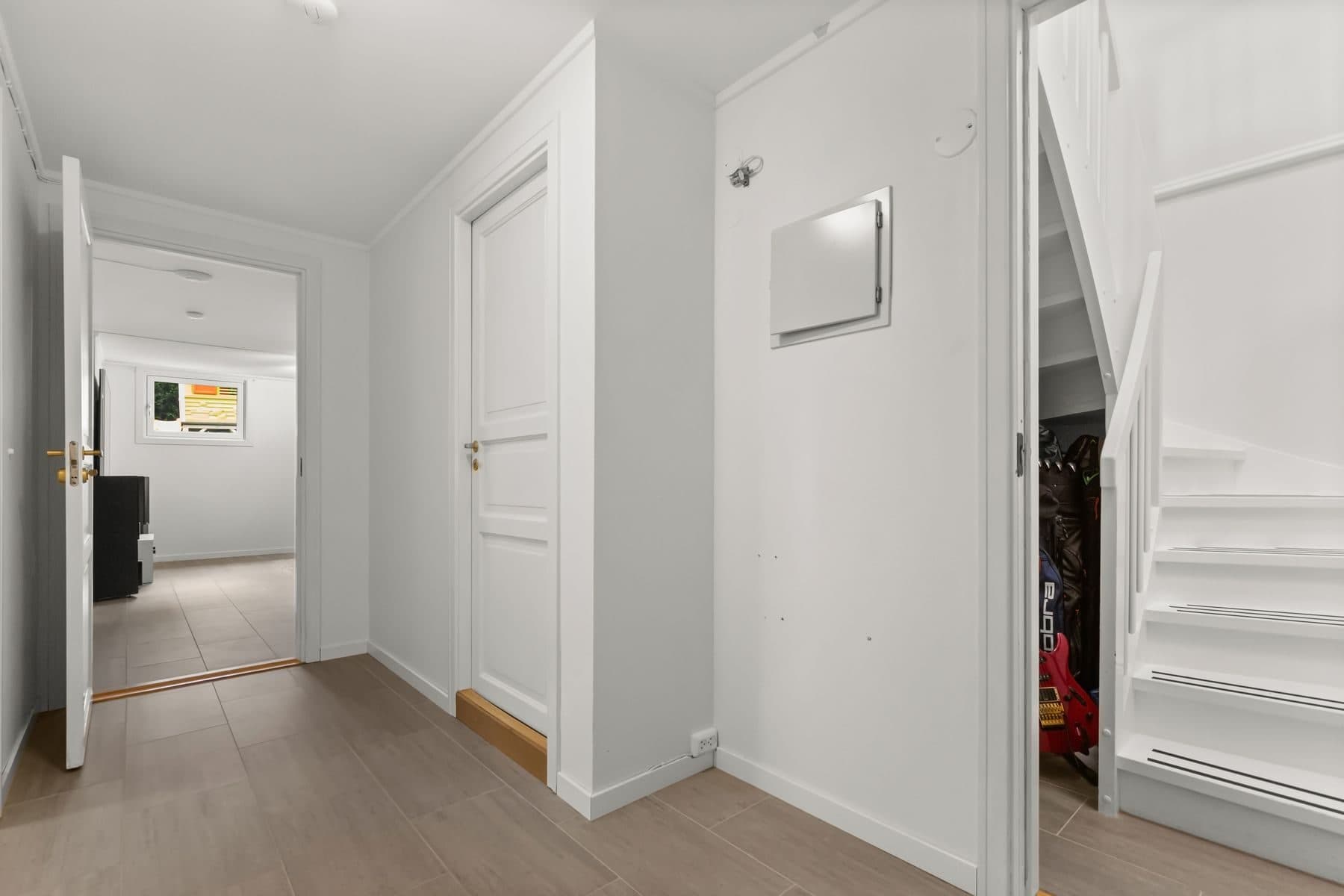 A bright white corridor with white doors, a stair and a light wood floor.