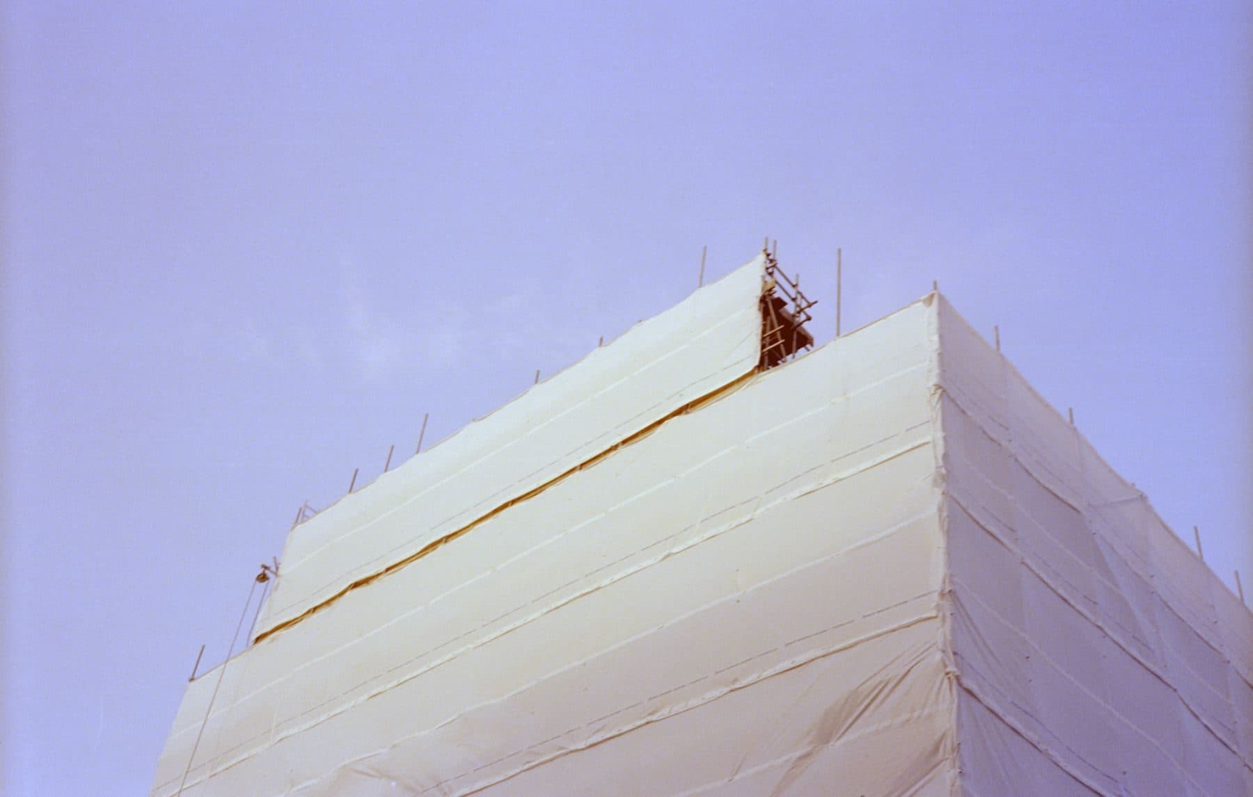 A building wrapped in white protective sheeting over scaffolding.