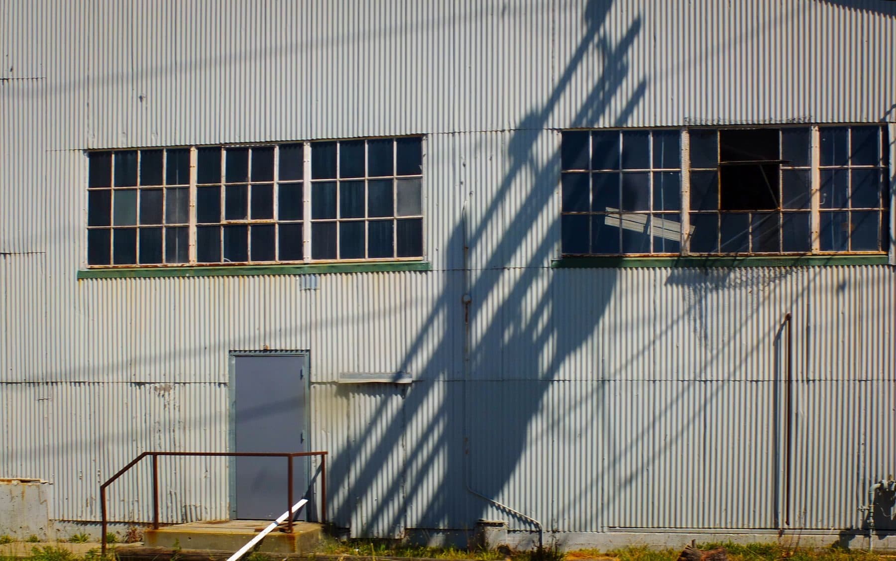 The corrugated metal side of an industrial building with steel-framed windows.